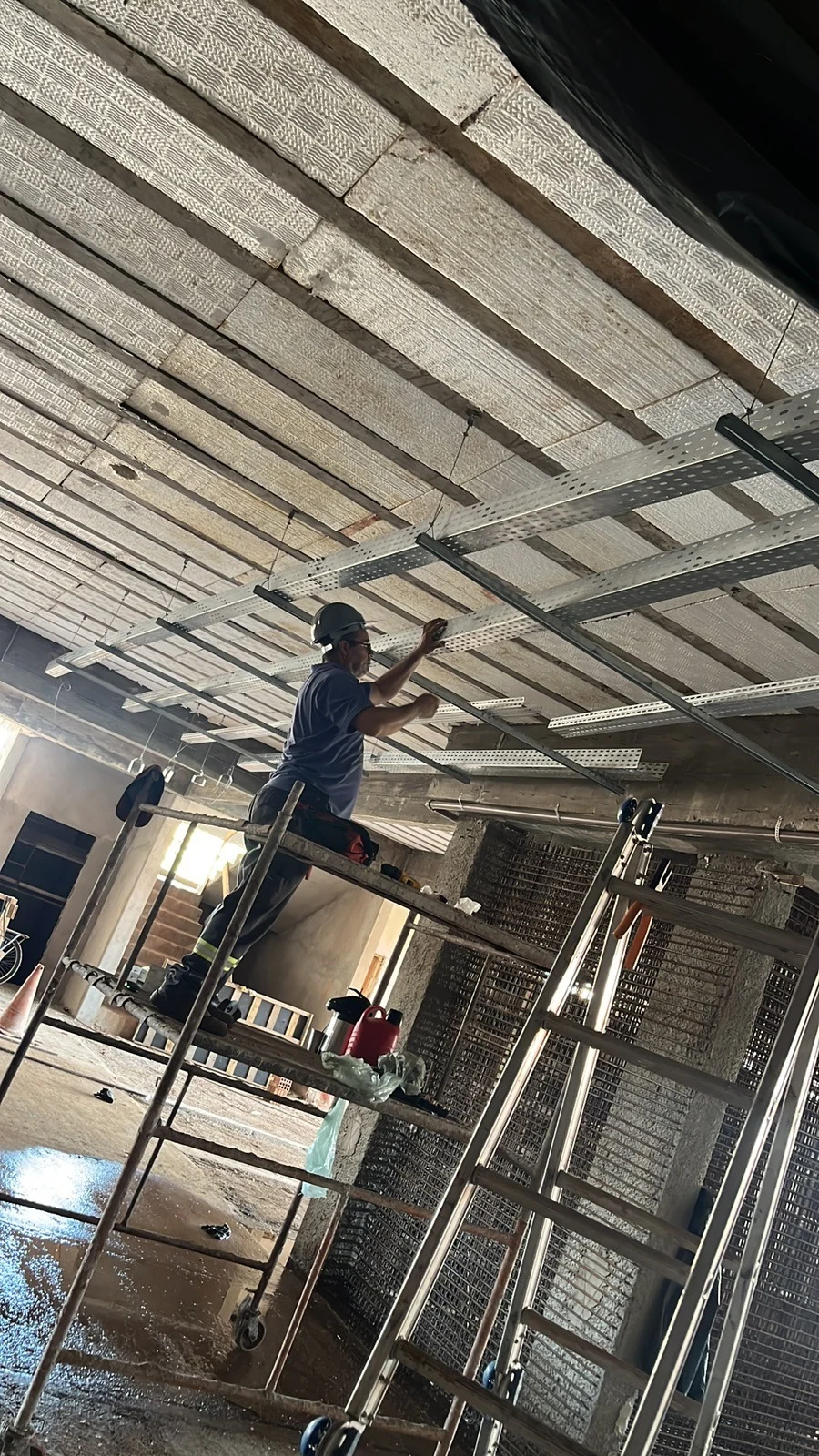 Eletricista da AEGIS montando eletrocalha perfurada presa à laje durante a obra